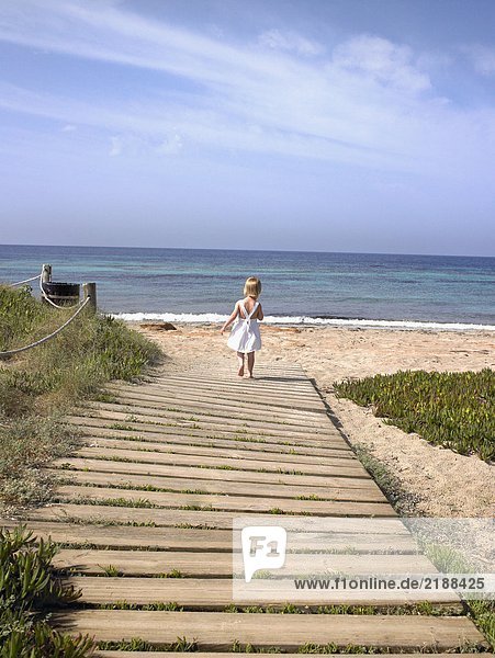 Young boy walking on a wooden path at the beach.