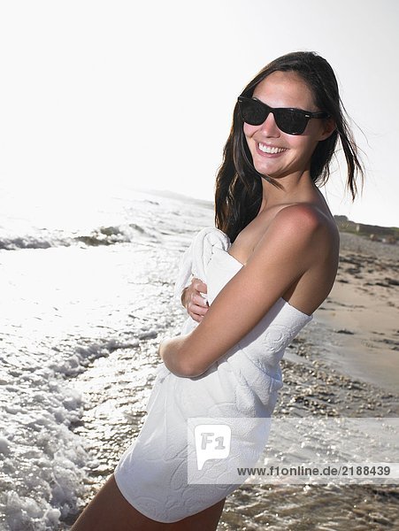 Frau steht in einem Handtuch am Strand und lächelt.