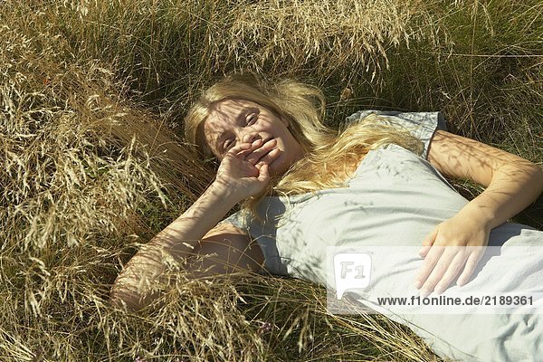 Junge Frau im langen Gras liegend.