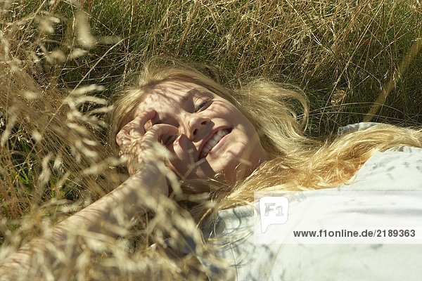 Junge Frau im langen Gras liegend.