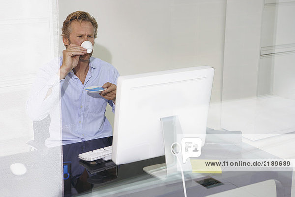 Man at computer drinking Espresso with reflections.