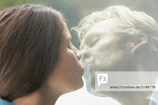 Ein junges Paar  das sich durch ein Glas Fenster küsst.