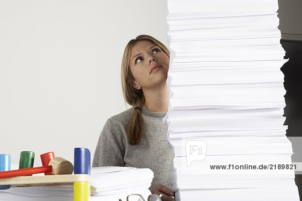 Young woman working from home with huge pile of paper.