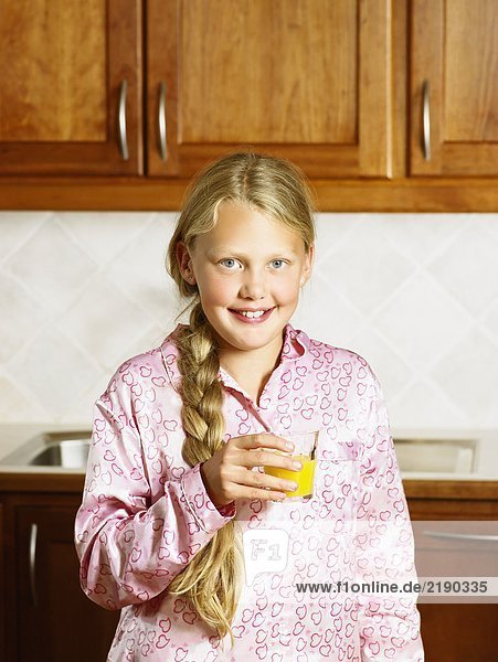 Young girl holding orange juice in kitchen smiling.