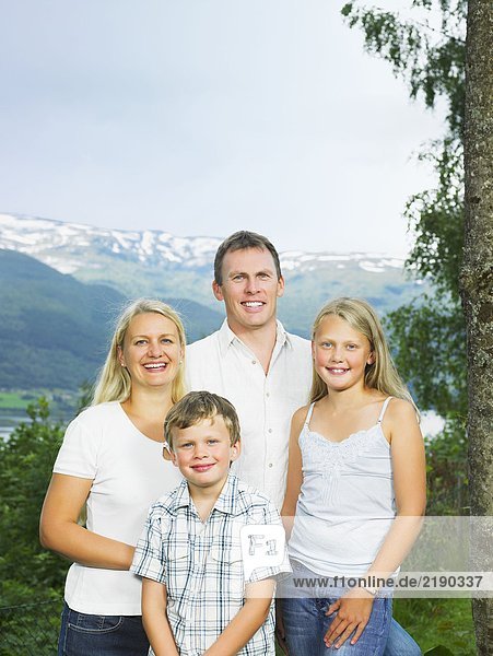 Familie im Freien durch hohen Baum lächelnd.