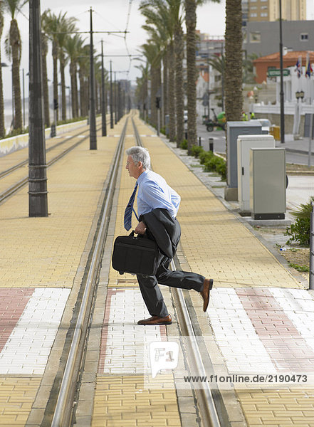 Senior Geschäftsmann  der mit der Straßenbahn über den Fußgängerüberweg läuft.