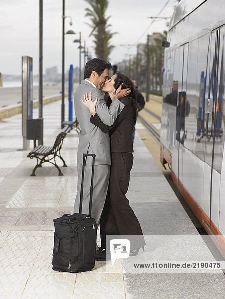 Couple wearing business suits kissing each other on platform next to static train/tram