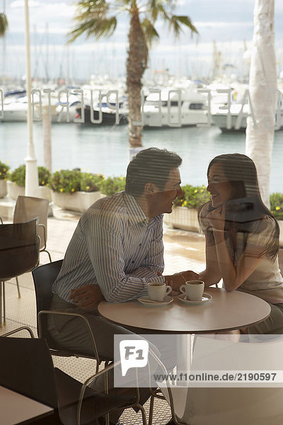 Loving couple sitting outside café by harbour shot through window Alicante  Spain.
