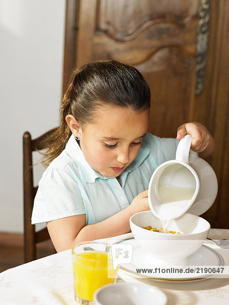 Mädchen (4-6) beim Frühstück Milch auf Müsli gießen