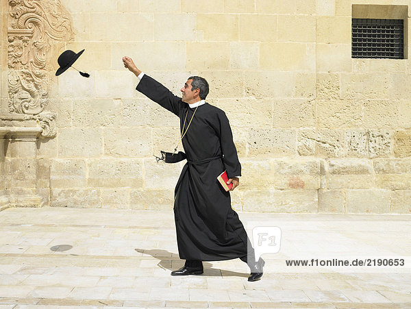 Priester  der nach seinem Hut greift  der im Wind weht  Alicante  Spanien