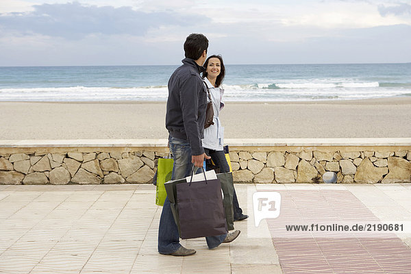 Young couple carrying shopping walking on promenade by beach