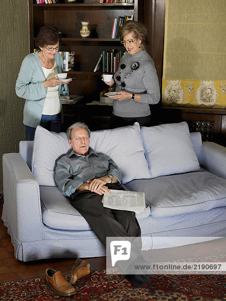 Two senior women drinking tea behind sofa while senior man dozes. Alicante  Spain.