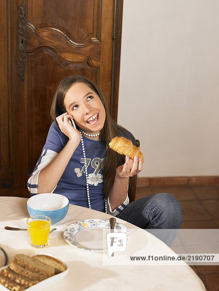 Girl (12-14) talking on phone at breakfast table
