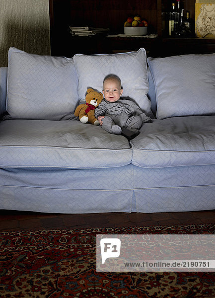 Baby boy (1-3 months) sitting on sofa illuminated by television