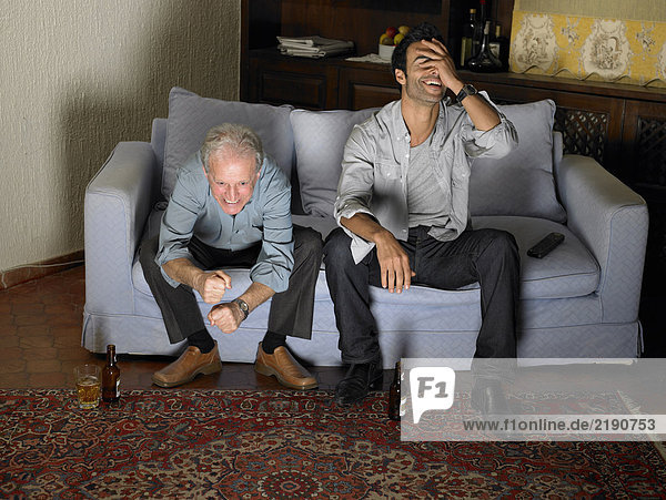 Senior father and son sitting on sofa watching television