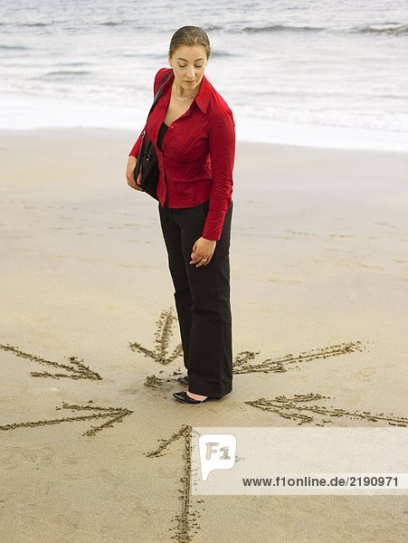 Woman on beach with arrows in sand around her.