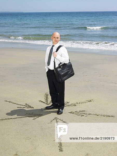 Mann am Strand mit Pfeilen im Sand um ihn herum.