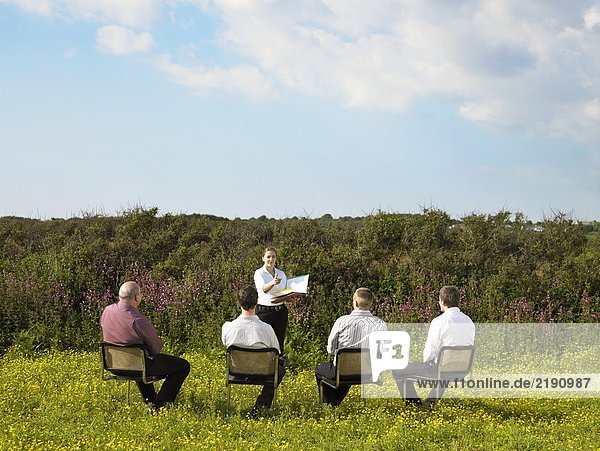 Gruppe von Geschäftsleuten  die auf Stühlen im Feld sitzen.