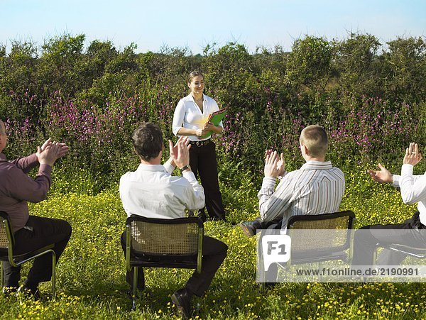 Gruppe von Geschäftsleuten  die auf Stühlen im Feld sitzen.