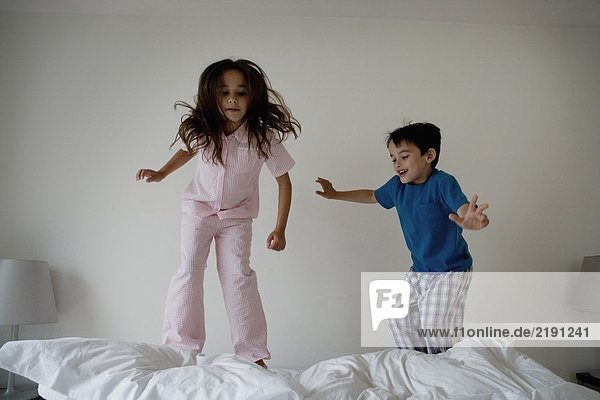 Girl and boy jumping on a bed.