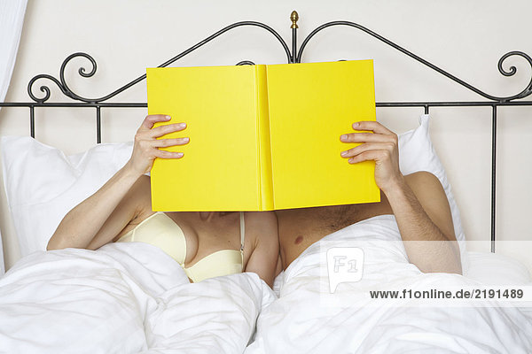 junges Paar im Bett hält gelbes Buch zusammen.