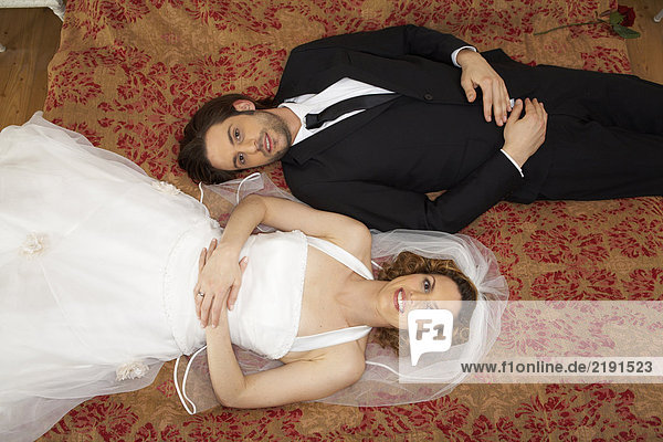 young bridal couple smiling lying on bed  overhead view  portrait