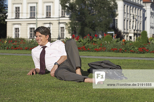 Businessman on square sitting in meadow laughing.