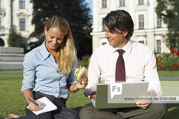 Businessman and businesswoman sitting in field working together.