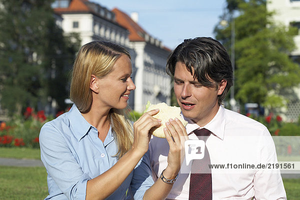Businesswoman feeding sandwich to businessman.