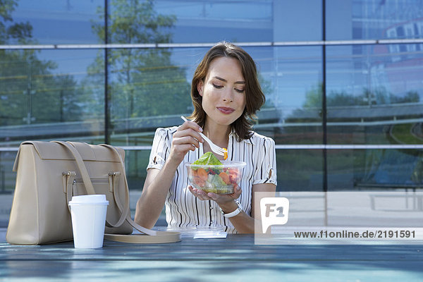 Geschäftsfrau auf dem Tisch vor dem Büro  die draußen Salat isst  um zu lachen.