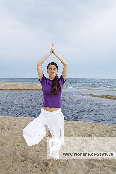 Frau beim Yoga am Strand mit geschlossenen Augen.