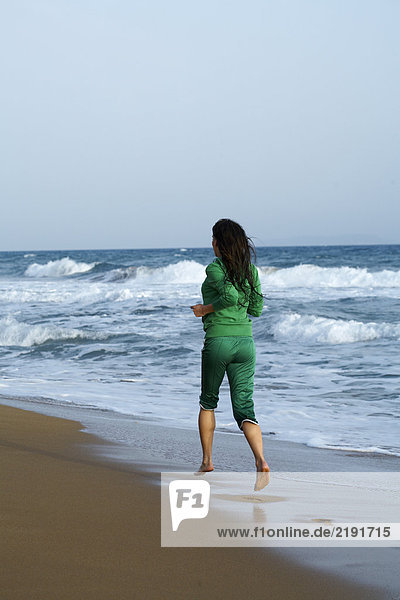 Frau  die am Strand vor der Kamera joggt.