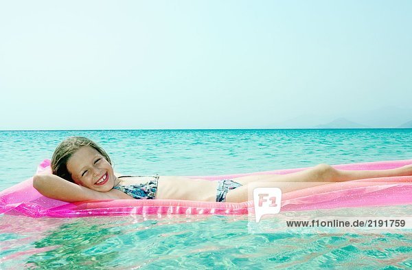 Young girl lying on inflatable raft in the water smiling.