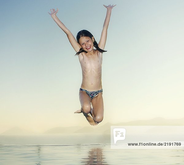 Young girl jumping into an infinity pool smiling.