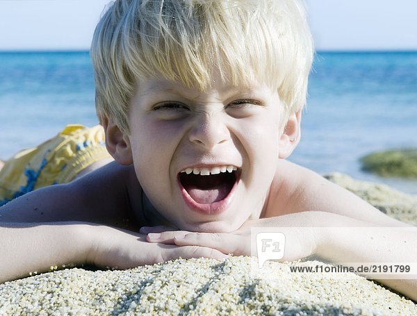 Young boy lying in the sand at the beach yelling.
