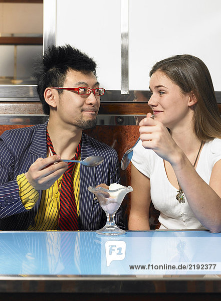 Young couple sharing icecream in cafe smiling at each other