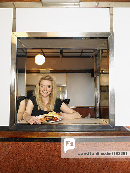 Kellnerin hält Teller mit frittiertem Essen an der Theke lächelnd