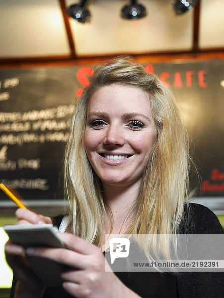 Junge Kellnerin mit Notizblock im Café lächelnd Portrait