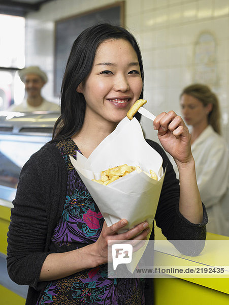 Young woman eating chips in fish and chip shop smiling  portrait