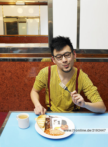Junger Mann  der allein im Diner frittiertes Essen isst.