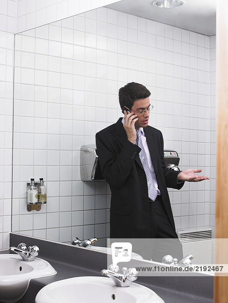 Der Mensch spiegelt sich im Büro-Waschraumspiegel mit dem Handy wider.