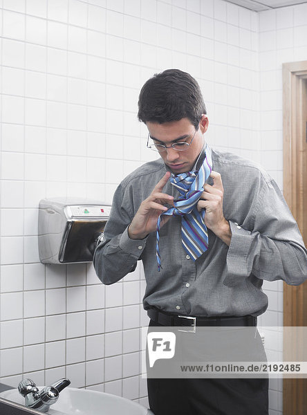 Man reflected in office washroom mirror doing up his tie