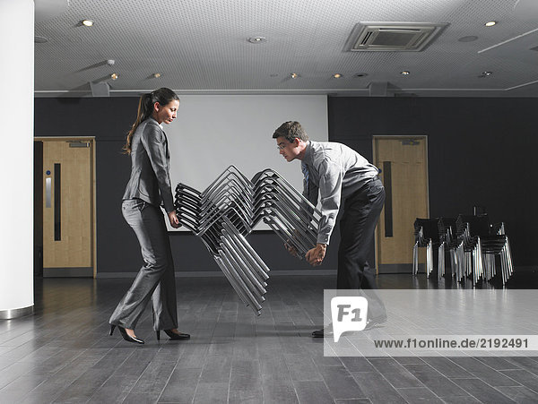 Man and woman moving stack of chairs in empty presentation room