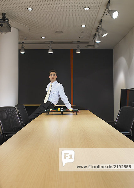 Porträt eines jungen Mannes am Konferenztisch mit Miniatur-Tischtennis-Set