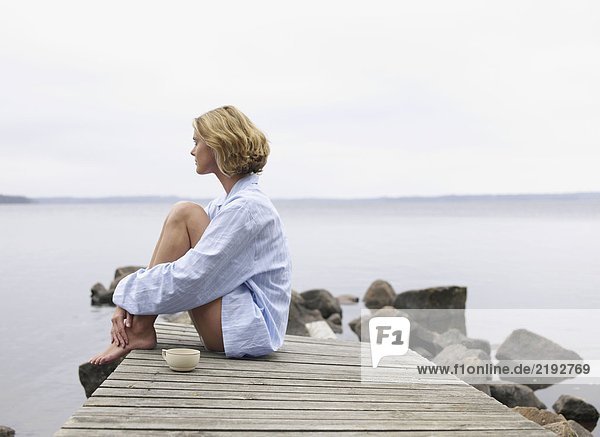 Frau mit geschlossenen Augen sitzend auf einem Dock mit einem Becher.