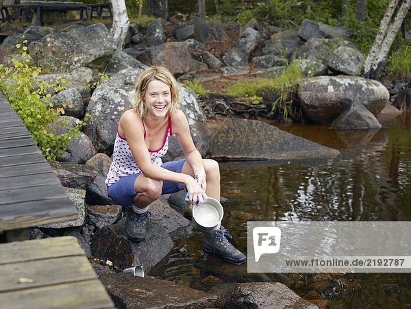 Frau wäscht eine Schüssel im Wasser bei einem Dock lächelnd.