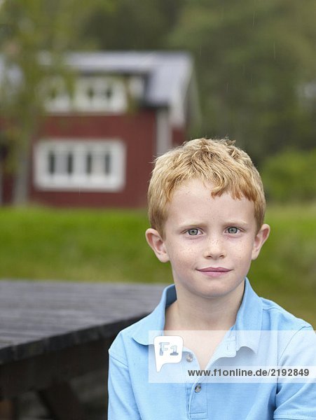 Kleiner Junge sitzt am Tisch im Freien mit Haus im Hintergrund.