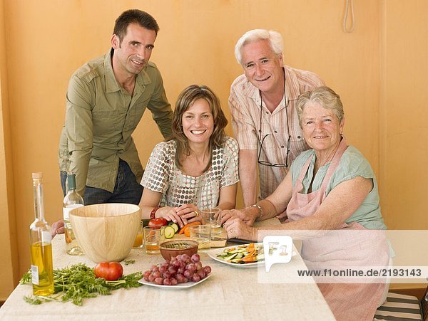 Seniorenpaar bei der Zubereitung des Essens zu Hause mit erwachsenen Nachkommen lächelnd Portrait