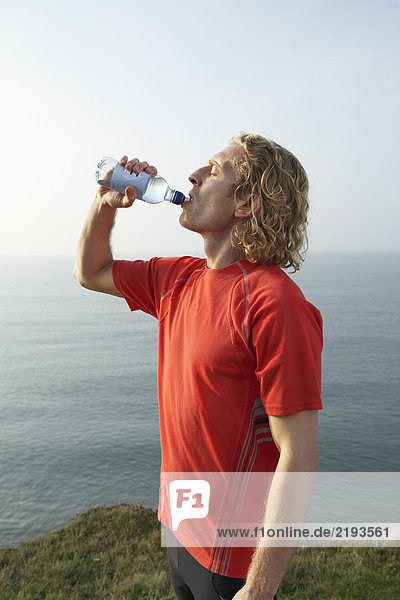 Ein junger männlicher Läufer trinkt aus einer Flasche.