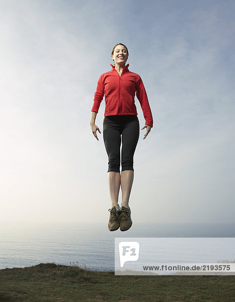 Eine Frau  die gegen eine Meereslandschaft springt.